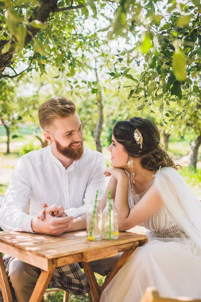 Attractive couple newlyweds, happy and joyful moment. bride and groom sit at table set for two in woods. Concept romantic date. Wedding couple sitting in cafe table and lovingly look at each other