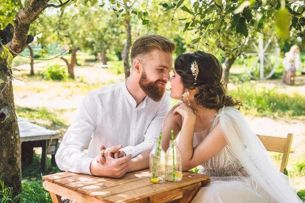 Attractive couple newlyweds, happy and joyful moment. bride and groom sit at table set for two in woods. Concept romantic date. Wedding couple sitting in cafe table and lovingly look at each other