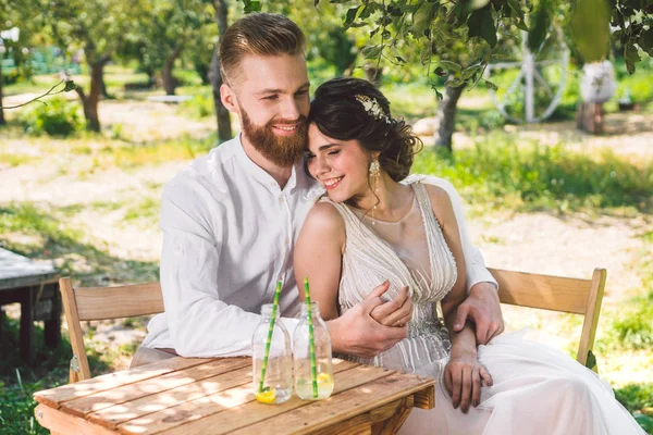 Çekici çift yeni evliler, mutlu ve neşeli an. gelin ve damat ormanda iki için belirlenen masada oturup. Kavram romantik tarih. Düğün çift kafe masada oturan ve sevgiyle birbirlerine bakmak