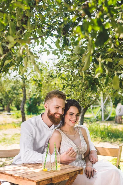 Çekici çift yeni evliler, mutlu ve neşeli an. gelin ve damat ormanda iki için belirlenen masada oturup. Kavram romantik tarih. Düğün çift kafe masada oturan ve sevgiyle birbirlerine bakmak