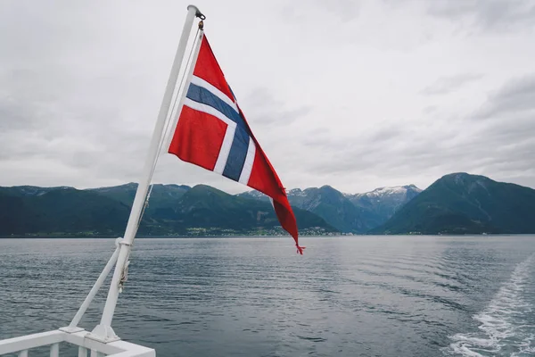 Norveç bayrağı geminin korkuluklarında sallanıyor ve suyun üzerinde sallanıyor. Bayrağı olan Norveç fiyordu. Norveç 'e feribot yolculuğu. Denizde ve dağlarda Norveç Bayrağı