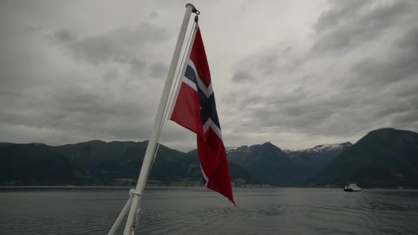 Norveç bayrağı geminin korkuluklarında sallanıyor ve suyun üzerinde sallanıyor. Bayrağı olan Norveç fiyordu. Norveç 'e feribot yolculuğu. Denizde ve dağlarda Norveç Bayrağı — Stok video