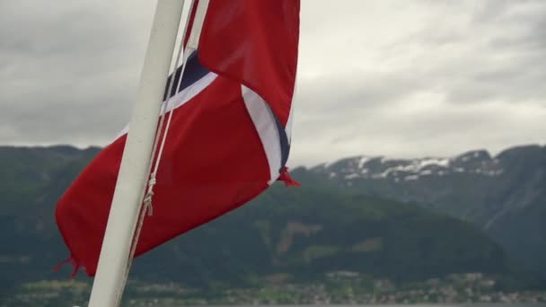 Norveç bayrağı geminin korkuluklarında sallanıyor ve suyun üzerinde sallanıyor. Bayrağı olan Norveç fiyordu. Norveç 'e feribot yolculuğu. Denizde ve dağlarda Norveç Bayrağı — Stok video