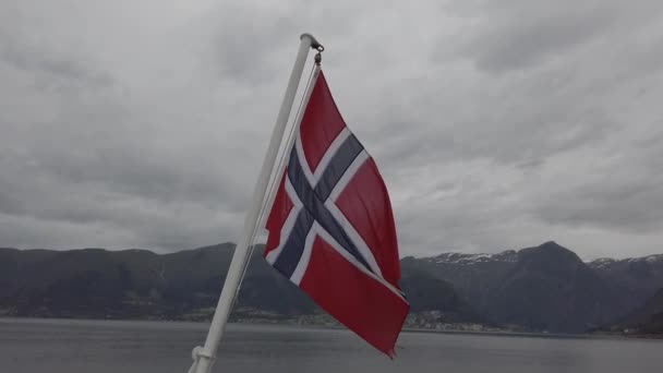 Norweska flaga wisząca na balustradzie statku i machająca nad wodą. Norweski fiord z flagą. Prom w Norwegii. Flaga Norwegii na tle morza i gór — Wideo stockowe