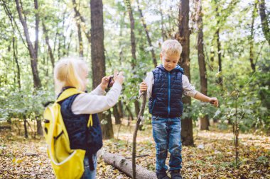Çocuk okul öncesi Kafkas erkek ve kız kardeşi Forest Park sonbaharda cep telefonu kamerası birbirlerinin fotoğraflarını çekmek. çocuk için hobi ve aktif yaşam tarzı teması. Meslek fotoğrafçısı