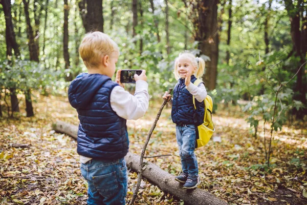 Kinder im Vorschulalter fotografieren sich gegenseitig mit der Handykamera im Waldparkherbst. Thema Hobby und aktiver Lebensstil für Kinder. Beruf Fotograf — Stockfoto