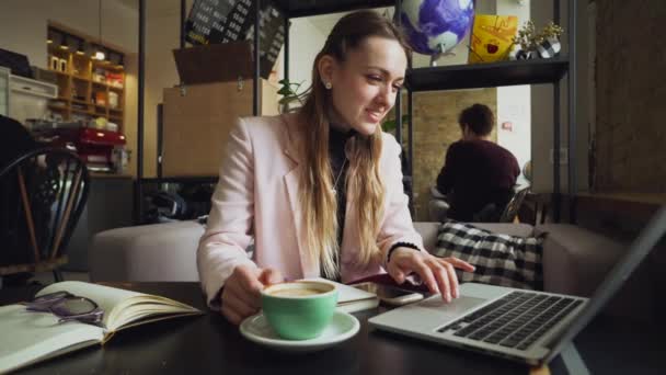 Mulher branca bonita bebendo café e digitando em um teclado dentro de um café em uma mesa de madeira. O tema das profissões modernas é um blogueiro, freelancer e escritor — Vídeo de Stock