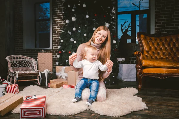 Joven madre e hijo jugando cerca del árbol de Navidad. joven madre e hijo jugando cerca del árbol de Navidad. Noche de Navidad familiar. Mamá e hijo en piso alfombra peluda bajo el árbol de Navidad — Foto de Stock