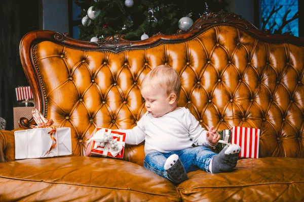 Boldog kis mosolygó fiú karácsonyi ajándékdobozban. Gyönyörű kis bébi, ül asofa ajándékkal. Gyermek ül egy halom karácsonyi ajándékokat. Karácsonyi ajándékkoncepció — Stock Fotó