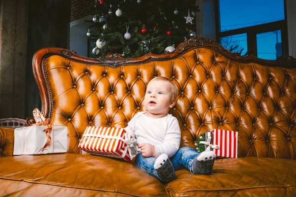 Ευτυχισμένο μικρό χαμογελαστή αγόρι με Χριστουγεννιάτικο κουτί δώρου. Ένα όμορφο μωράκι, κάθεται σε ένα δώρο. Το παιδί κάθεται δίπλα σε ένα σωρό Χριστουγεννιάτικα δώρα. Χριστουγεννιάτικη ιδέα δώρου — Φωτογραφία Αρχείου