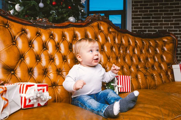 Feliz niño sonriente con caja de regalo de Navidad. Hermoso bebé, se sienta en asofa con regalo. Niño sentado junto a un montón de regalos de Navidad. concepto de regalo de Navidad — Foto de Stock