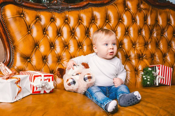 Feliz niño sonriente con caja de regalo de Navidad. Hermoso bebé, se sienta en asofa con regalo. Niño sentado junto a un montón de regalos de Navidad. concepto de regalo de Navidad — Foto de Stock