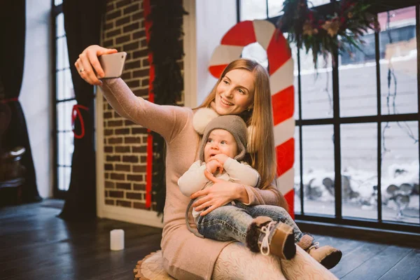 Navidad, tecnología y concepto familiar, madre feliz e hijo pequeño tomando teléfono inteligente selfie en casa. El niño y mamá hacen selfie en el teléfono móvil. madre e hijo hace foto autorretrato en invierno — Foto de Stock