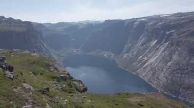 26 Temmuz 2019. Norveç. Hayalperest bir adam kayanın üzerinde uzanmış, arka planda mavi su fiyorduyla yamaçta yürüyüş yaptıktan sonra dinleniyor. Norveç gezisi, özgürlük konsepti. En tepedeki turist telefon kullanıyor
