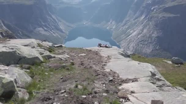 26 de julio de 2019. Noruega. hombre soñador acostado en piedra, relajarse después de caminar en la cima de la montaña acantilado con fiordo de agua azul en el fondo. Viaje a Noruega, concepto de libertad. turista en la montaña superior utiliza el teléfono — Vídeo de stock