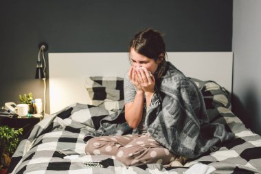 Burnu akan hasta bir kadın, yatakta oturuyor. Kadın kendini iyi hissetmiyor ve hapşırıyor. Elinde doku tutan bir kadın, grip belirtileri. Sağlık hizmeti tıbbi konsepti. Soğuk ve soğuk algınlığı mevsimi. Alerjisi olan kadın.