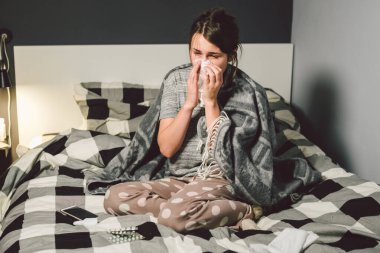 Burnu akan hasta bir kadın, yatakta oturuyor. Kadın kendini iyi hissetmiyor ve hapşırıyor. Elinde doku tutan bir kadın, grip belirtileri. Sağlık hizmeti tıbbi konsepti. Soğuk ve soğuk algınlığı mevsimi. Alerjisi olan kadın.