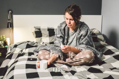 Mevsimlik soğuk, burun akıntısı grip virüsü enfeksiyonu temasıdır. Genç beyaz bir kadın kaydırma battaniye oturan ev yatak odası yatak chill ısı yüksek sıcaklığı. Bardak içki hapları sezon gribi blister