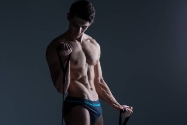 Kas Fitness genç erkek antika mükemmel kaslar altı paketleri ABS ve çıplak göğüs. Stüdyodan karanlık bir arka plana karşı streç elastik ile vücut geliştirmeci Model trenler. Egzersiz eğitim spor salonu