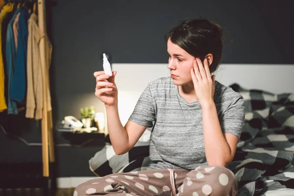 The theme is seasonal cold, runny nose flu virus infection. Young caucasian woman at home bedroom bed uses spray drops of medicine in her nose for snot. Allergic renitis and sinusitis — Stock Photo, Image