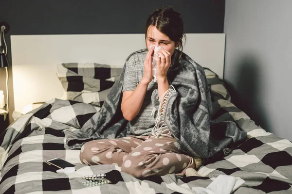 Mujer enferma con secreción nasal, sentada en la cama. mujer sintiéndose mal y estornudar dormitorio. Mujer sosteniendo tejido, síntomas de gripe. Concepto médico de salud. Temporada Fría y Gripe. mujer con síntomas de alergia —  Fotos de Stock