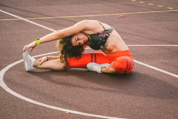 Woman Athlete Stretching Legs On Stadium. Female Runner Stretching Before Workout. Lifestyle portrait of athletic girl doing warm up and workout and stretching. Confident Young Woman Warming Up