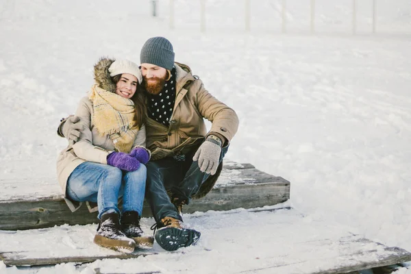 Älskade par unga människor en man med skägg och en vit kvinna sitter på en trätrappa på vintern på snön St. Alla hjärtans dag en dag jul kramas och glad — Stockfoto
