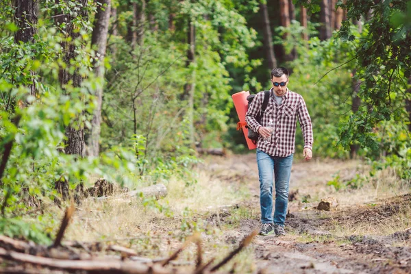 Young man walking in forest. He exploring forest, enjoy in autumn day, holding bottle in outdoor forest scenery. Adventures hiking. Outdoor lifestyle freedom concept. — Stock Photo, Image