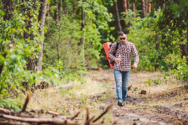 Young man walking in forest. He exploring forest, enjoy in autumn day, holding bottle in outdoor forest scenery. Adventures hiking. Outdoor lifestyle freedom concept.