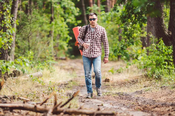 Young man walking in forest. He exploring forest, enjoy in autumn day, holding bottle in outdoor forest scenery. Adventures hiking. Outdoor lifestyle freedom concept.