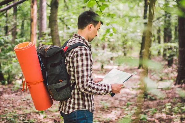 Homem com mochila e mapa procurando direções na área selvagem. Turista com mochila usando mapa na floresta. férias de turismo conceito. Caminhante. Homem viajante perdido caminhando na floresta olhando para o mapa — Fotografia de Stock