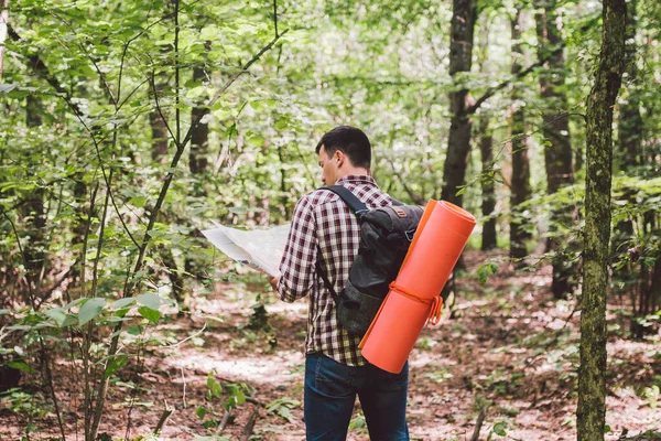 Muž s batohem a mapou hledající směr v divočině. Turista s batohem pomocí mapy v lese. koncepce turistických dovolených. Turista. Cestující muž ztratil procházky v lese při pohledu na mapu — Stock fotografie