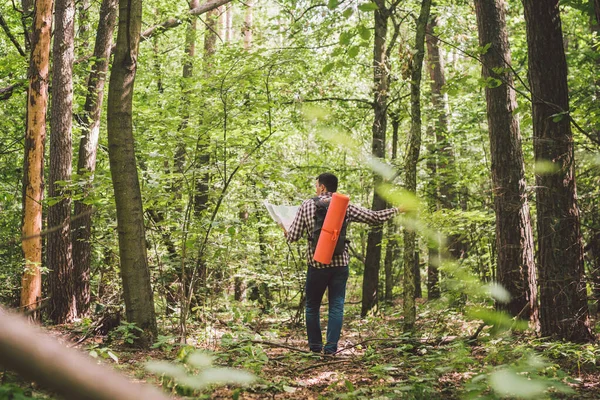 Man med ryggsäck och karta söka igenom vägbeskrivning i vildmarksområdet. Turist med ryggsäck med hjälp av karta i skogen. koncept turism semester. Vandringsman. Resande man vilse promenader i skogen tittar på kartan — Stockfoto