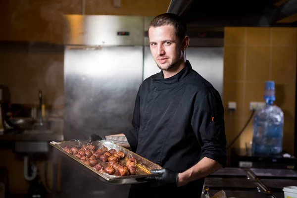 Portret mannelijke chef-kok met gekookt eten in de keuken. Themakoken. Jonge blanke man in zwart uniform, latex handschoenen in restaurant in keuken. schaal van vijgen, vijgenfruitvijgenboom of Ficus Carian — Stockfoto
