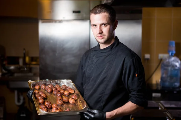 Portrait male chef with cooked food standing in kitchen. Theme cooking. young Caucasian man in black uniform, latex gloves at restaurant in kitchen. dish of figs, fig fruit fig tree or Ficus Carian