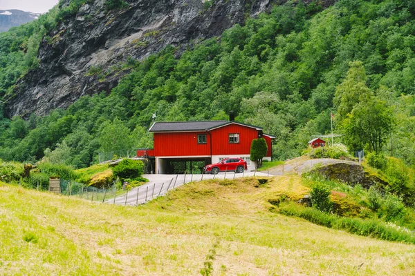 Červený dřevěný dům a auta v norském městě Flam. Venkovský dům a auto na dvoře. Chaty v horách. — Stock fotografie