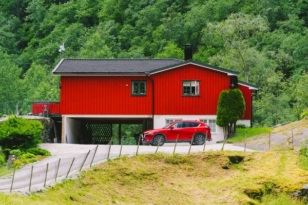 Červený dřevěný dům a auta v norském městě Flam. Venkovský dům a auto na dvoře. Chaty v horách. — Stock fotografie