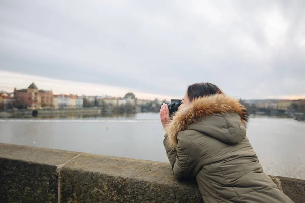 La mujer está tomando fotos en el puente Charles en Praga. Joven hermosa chica turística se para en el Puente de Carlos en Praga en la República Checa y toma fotos de hermosas vistas de la ciudad — Foto de Stock