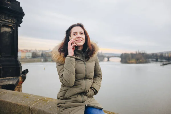 スマートフォンで話すプラハの観光客の女性を笑顔。チェコ共和国のカレル橋に立つ若い女性観光客は電話を使用しています — ストック写真