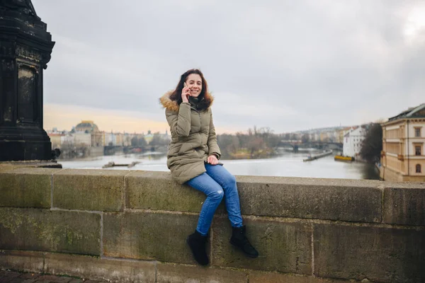 在布拉格用智能手机微笑的女游客。 捷克共和国布拉格查尔斯桥上的年轻女性游客站在电话旁 — 图库照片