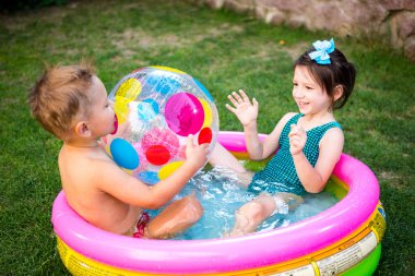 Küçük çocuklar yüzme havuzunda evin avlusunda büyük şişme plaj topu oynarlar. Sıcak ve su oyunları, yaz tatilleri ve tatiller teması. Açık havuzda banyo yapan komik çocuklar..