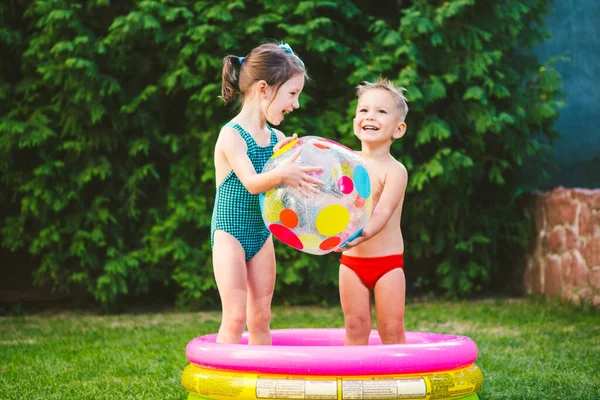 スイミングプールでビーチボールを持つ2人の子供 裏庭の膨脹可能なプールで遊ぶ楽しい子供 晴れた日にプールで小さな子供たち カラフルなスイミングプールボール 健康な赤ちゃんの夏の活動 — ストック写真