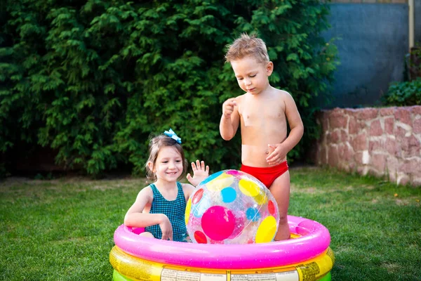 子供ゲームのためのおもちゃ 子供たちはインフレータブルゴムビーチボールで遊んでいます 水のプールで 夏休みだ 少年少女はインフレータブルプール裏庭で遊んでいます 夏の庭で外で遊んでいる子供たち — ストック写真