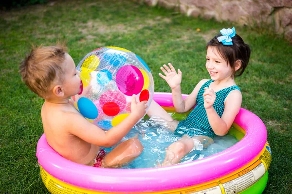 Young children siblings play large inflatable beach ball in courtyard of house in swimming pool. theme of heat and water games, summer holidays and vacations. Funny children bathing in outdoor pool.
