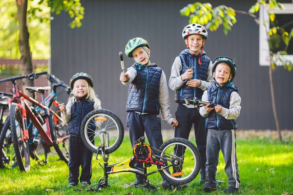 Children mechanics, bicycle repair. Happy kids fixing bike together outdoors in sunny day. Bicycle repair concept. Teamwork family posing with tools for repairing a bicycle in hands outside.