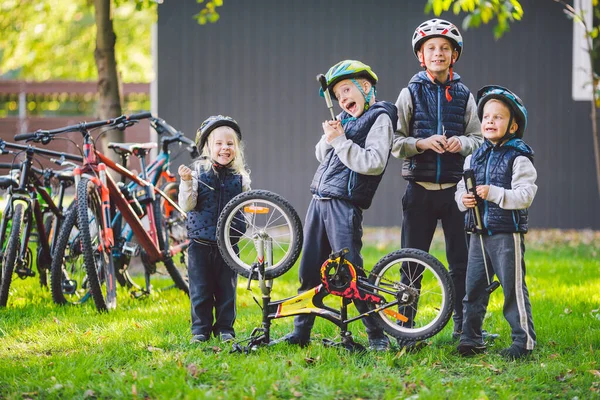 Children mechanics, bicycle repair. Happy kids fixing bike together outdoors in sunny day. Bicycle repair concept. Teamwork family posing with tools for repairing a bicycle in hands outside.