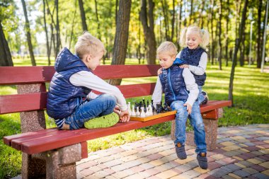 Parktaki bankta satranç oynayan küçük okul çocukları. Yaz tatilleri, entelektüel oyunlar. Çocuklar için satranç kulübü. Mutlu çocukluk ve çocukların arkadaşlığı. Beyin gelişimi için mantık oyunu.