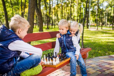 Küçük kardeşler parkta kız kardeşiyle satranç oynuyorlar. Çocuk istihbaratı gelişimi. Aile eğlence zamanı. Çocuklar açık havada satranç oynuyorlar. Çocuk satranç kombinasyonları üzerinde çok düşünüyor..
