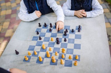 Eğitim konsepti, entelektüel oyun. Satranç turnuvası, ders, kamp, eğitim konsepti. Şehir parkındaki bir masanın üzerine çizilmiş satranç tahtasıyla oynayan çocukların yakın çekimi. Şehirde açık havada satranç.