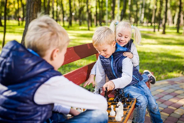 白人の子供たちは公園のベンチで木製のチェスボードでチェスをする 兄弟姉妹の大きなフレンドリーなアクティブな精神的な家族は 晴れた日に休暇に時間を過ごします 子供のチェスクラブ チェススポーツ — ストック写真
